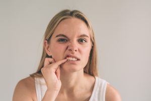 A horizontal photo of a young worried woman in checkered shirt suffering from strong toothache and touching her cheek