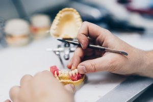 Dental prosthesis, prosthetics work. Close up of prosthetist hands while working on the denture. Selective focus.