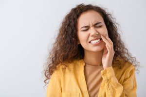 Beautiful young woman suffering from tooth ache on light background