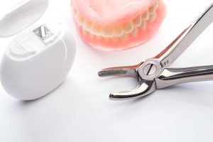 Teeth model with dental floss and forceps on white surface