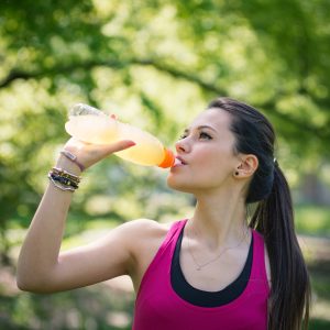 Young woman drinking energy drink outdoors in a park.