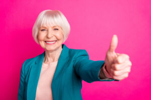 Close-up portrait of her she nice attractive cheerful content gray-haired lady wearing, blue green jacket showing giving thumbup isolated over bright vivid shine vibrant pink fuchsia color background