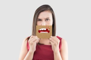 Asian woman in the red shirt holding a brown paper with the broken tooth cartoon picture of his mouth against the gray background, Decayed tooth, The concept with healthcare gums and teeth