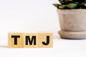 On a light background, wooden cubes with the inscription TMJ and a flower in a pot. Defocus