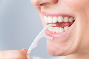 Caucasian woman brushing teeth with toothpick with dental floss on white background