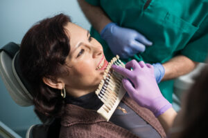 Dentist with assistant and female patient checking and selecting colour of the teeth in dental clinic office. Doctor is making the process of treatment. Dentistry