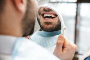 Cropped image of a handsome happy young man sitting in medical dentist center looking at mirror.