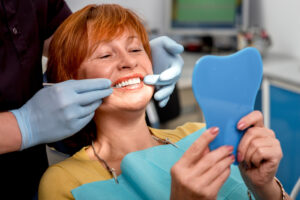 Smiling senior woman with new dental implants sitting in the dental office and looking at the mirror